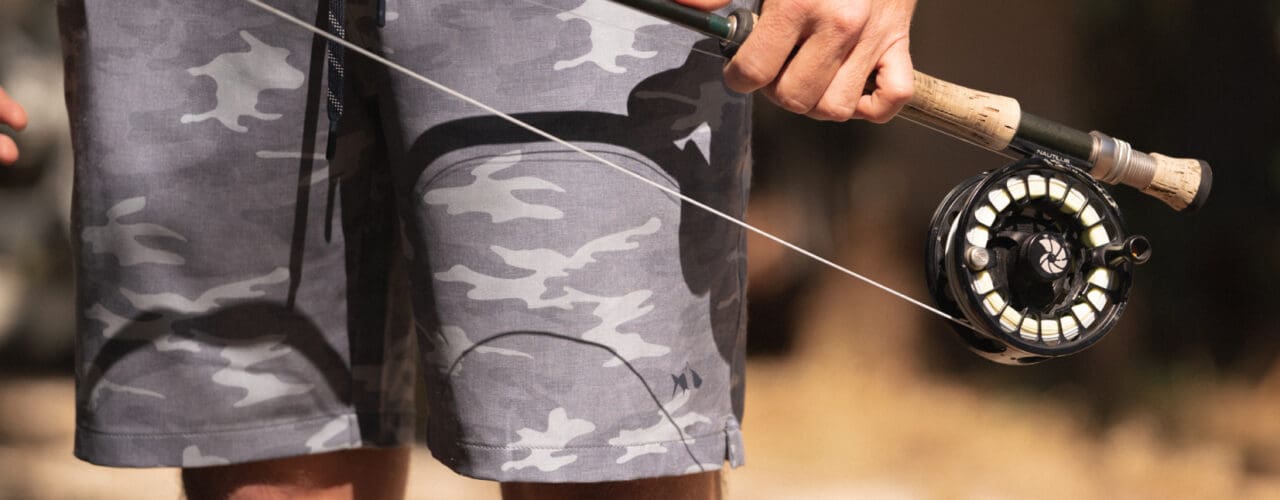 Man wearing shorts holding fly fishing rod